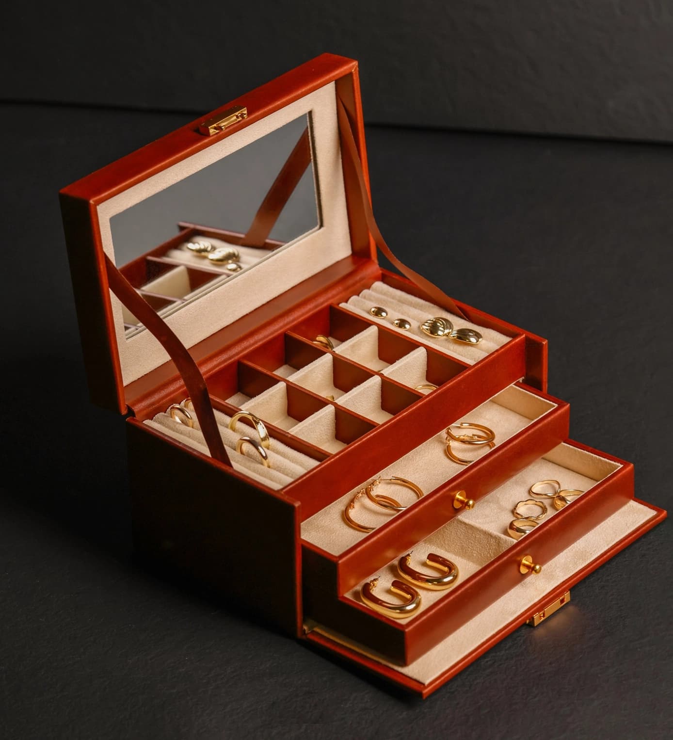 La Toletta open, cognac leather, mirror in the lid and two drawers of gold earrings.